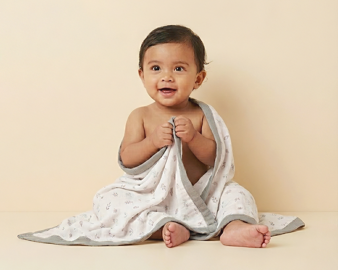 Baby wrapped in a white blanket with gray trim on a beige background